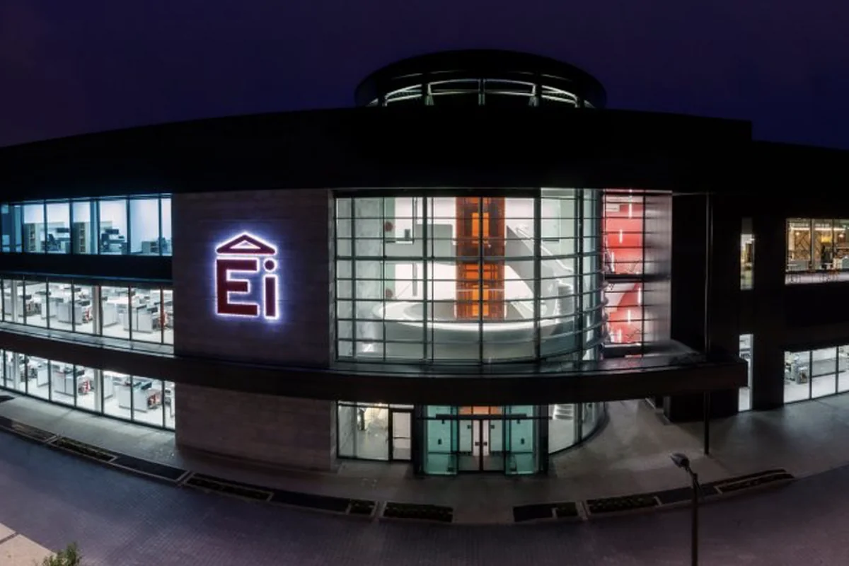 Ei Electronics' headquarters in Shannon at dusk — the curved glass frontage lit from inside, the Ei mark on the facade.